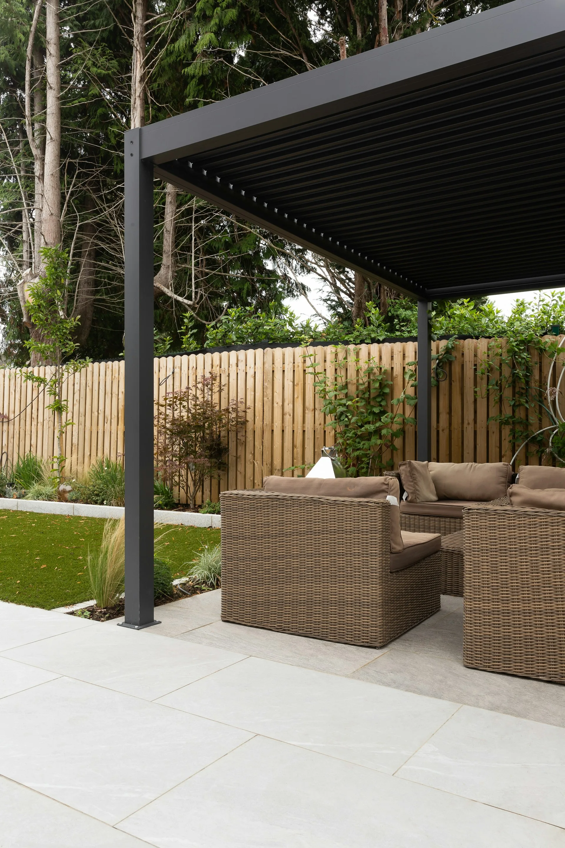 Mörk pergola med loungeplats i trädgård